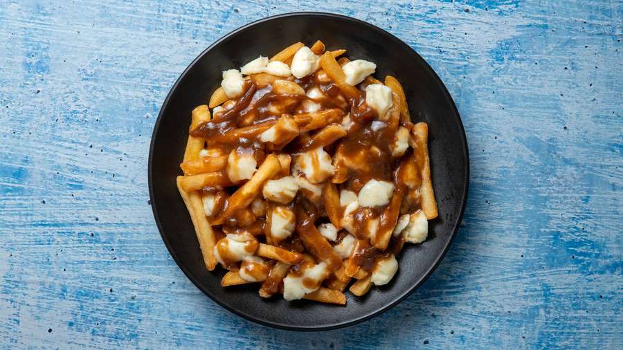 A plate of poutine with fries gravy and cheese curds on a blue background. — Poutine Wallpaper