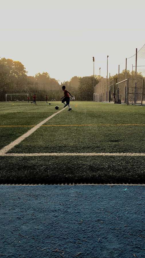 Young soccer player dribbling ball on turf field at sunset — Practical Picture