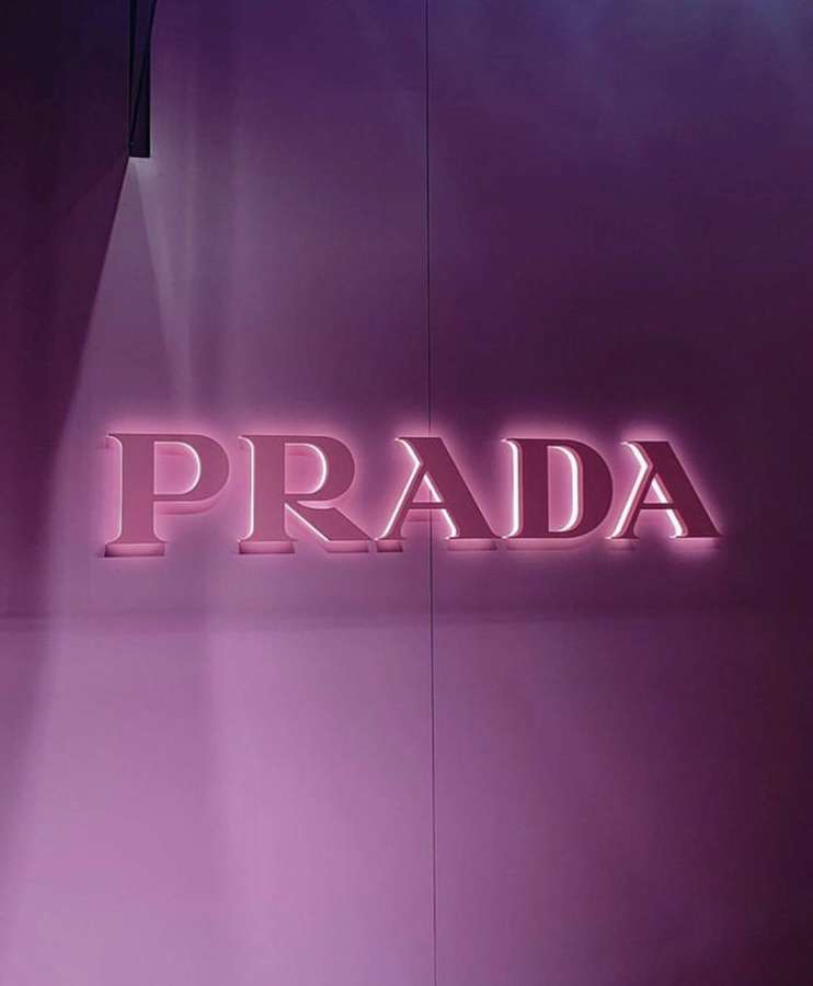 Prada-Logo in Pink vor einer lila Wand beleuchtet. — Prada Bilder
