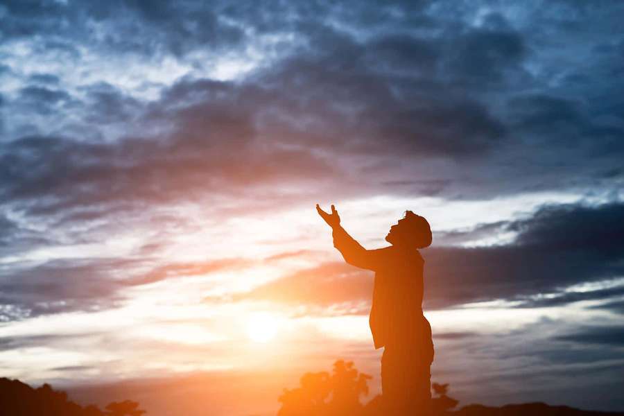 Person silhouetted against a vibrant sunset sky with arms raised in awe. — Praying Picture