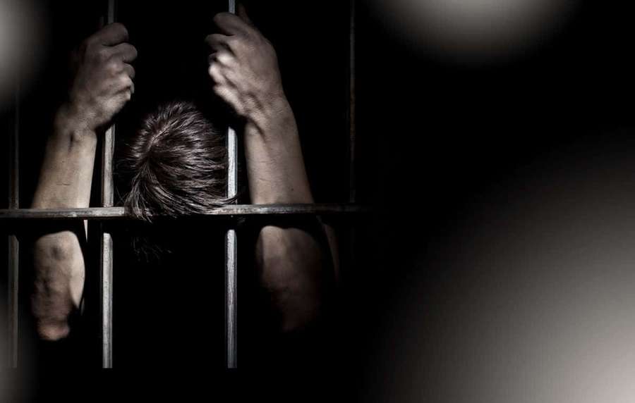 Person gripping prison bars with head down in darkness — Prison Background