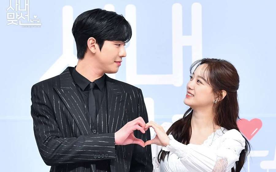 A man and woman smiling while making a heart shape with their hands at a press event. — Proposal Wallpaper