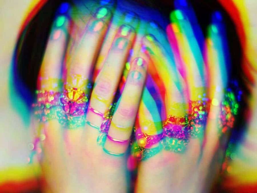 Hände mit Regenbogen-Glitzer-Nagelkunst bedecken Gesicht in farbenfroher Unschärfe. — Psychosomatic Wallpaper