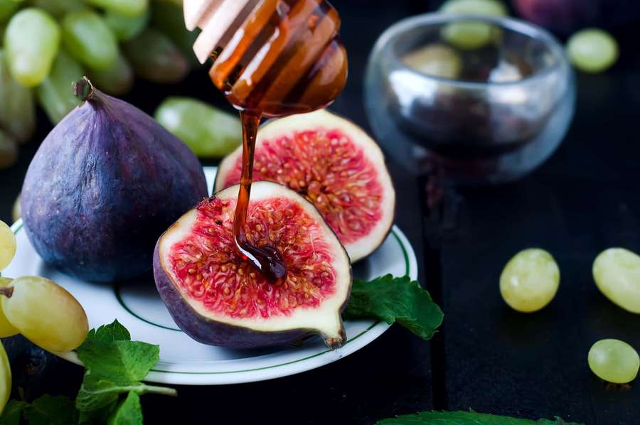 Honey drizzling onto a sliced fig with grapes and mint on a dark plate. — Purple Figs Wallpaper