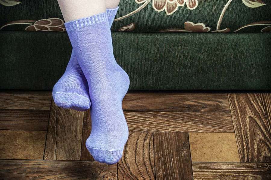 Feet in purple socks resting on wooden floor near green floral couch. — Purple Socks Wallpaper