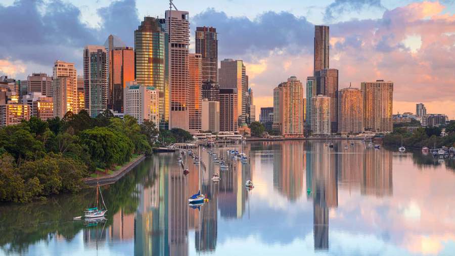 Horizonte de la ciudad al atardecer con barcos en aguas tranquilas y árboles verdes a lo largo de la orilla — Queensland Fondos de pantalla