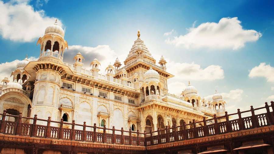 Grand ivory palace with domes and minarets under a bright blue sky with fluffy clouds. — Rajasthan Background