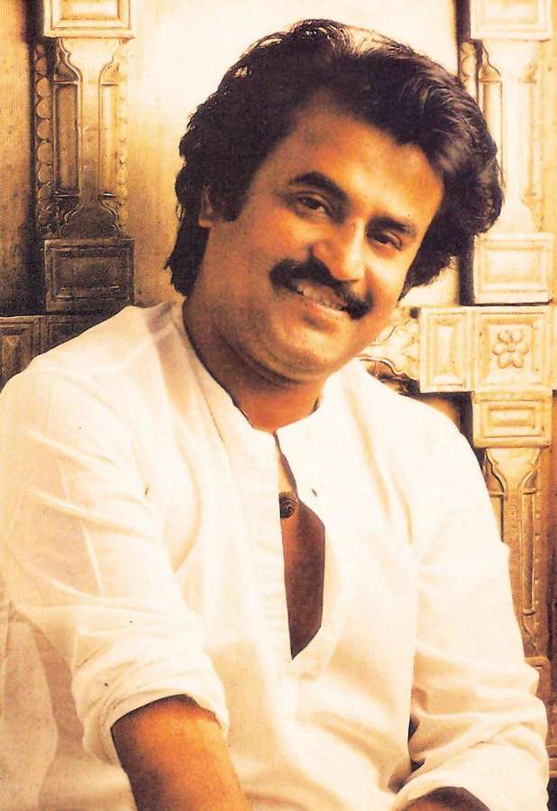 Man with mustache smiling in ornate golden room wearing white shirt. — Rajinikanth Background