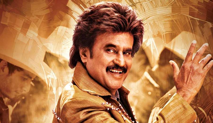 A smiling man in a gold jacket with a mustache against a warm abstract background. — Rajinikanth Wallpaper