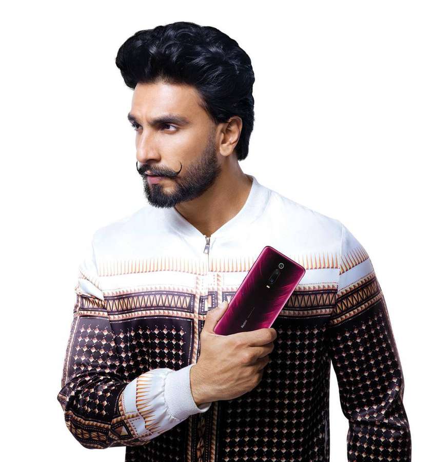 Man in patterned jacket holding magenta smartphone against white background. — Ranveer Singh Background