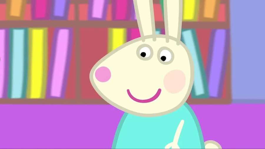 Cartoon rabbit smiling in front of a colorful bookshelf. — Rebecca Rabbit Wallpaper