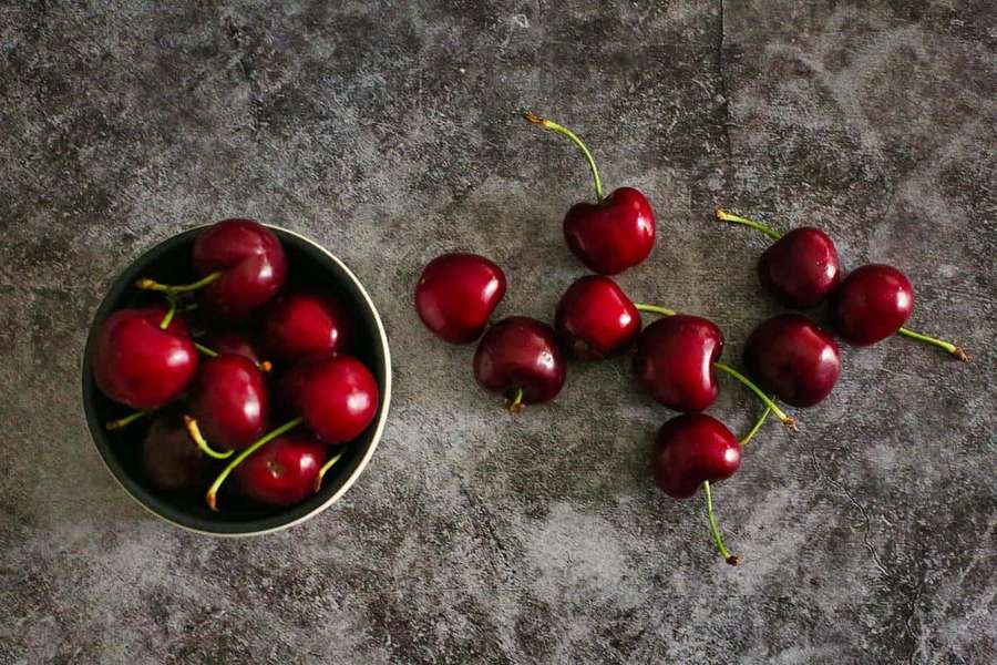 Fresh red cherries in a bowl and scattered on a gray stone surface. — Red Cherries Wallpaper