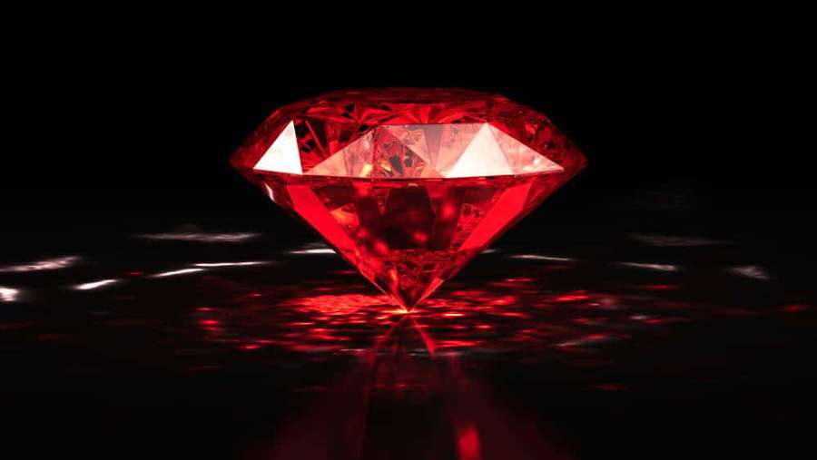 A radiant red diamond casting bright reflections on a dark surface. — Red Diamond Wallpaper