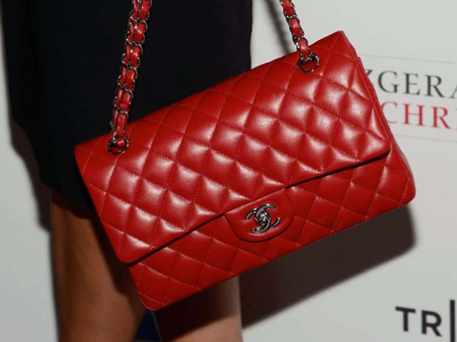 A red quilted Chanel handbag with silver chain strap worn by a person. — Red Handbag Wallpaper