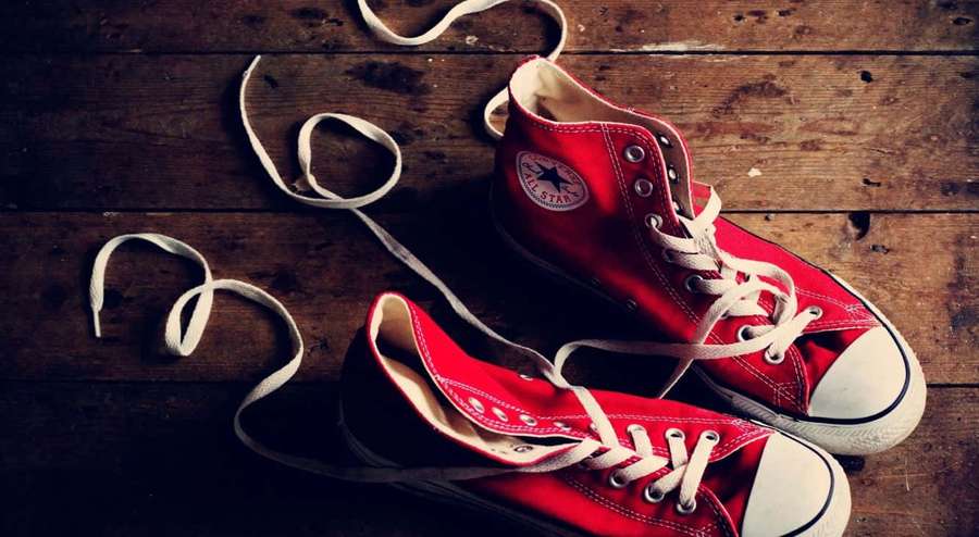 Red Converse sneakers with untied laces on a wooden floor. — Red Shoes Wallpaper