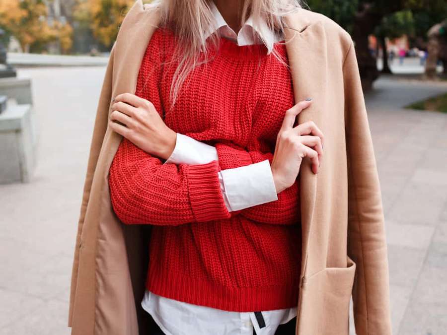 Person wearing red sweater and beige coat standing outdoors in autumn. — Red Sweater Wallpaper