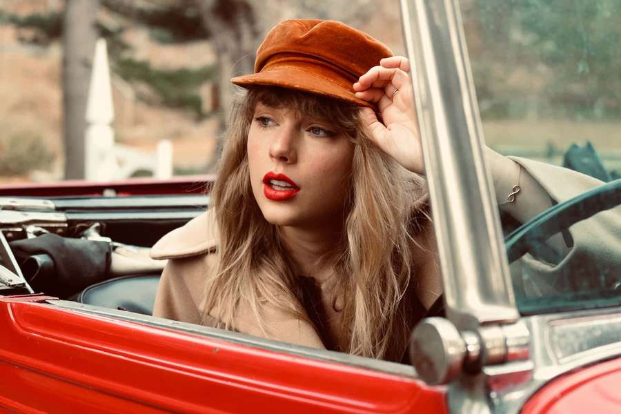 Woman in brown hat and beige coat leaning out of red vintage convertible car. — Red Taylors Version Wallpaper