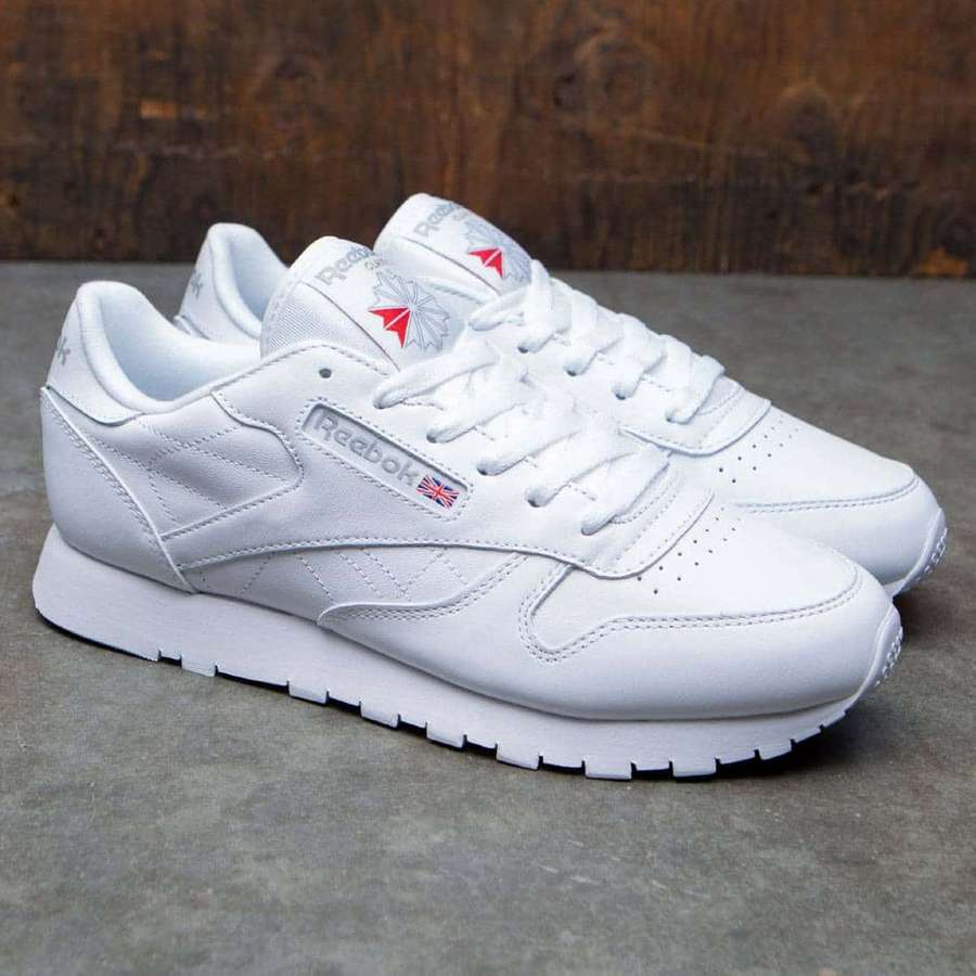 Weiße Reebok-Sneaker mit roten und blauen Details auf grauem Beton neben Holz. — Reebok Bilder