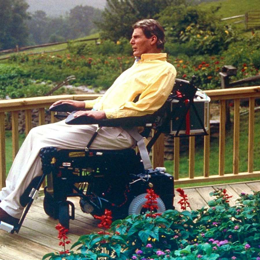 Man in yellow shirt in motorized wheelchair on wooden deck with colorful flowers — Reeve Wallpaper