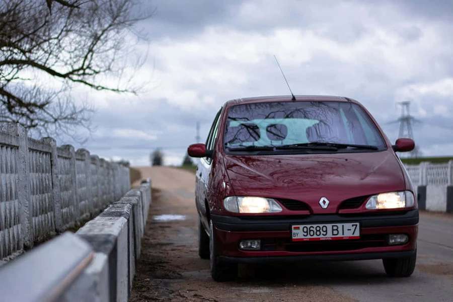Bordeauxrotes Auto auf Landstraße mit Betonbarriere und kahlen Bäumen unter bewölktem Himmel. — Renault Scenic Wallpaper