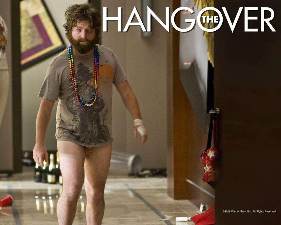 Un hombre con barba y cuentas camina por un pasillo de hotel desordenado después de una fiesta. — Resaca Fondos de pantalla