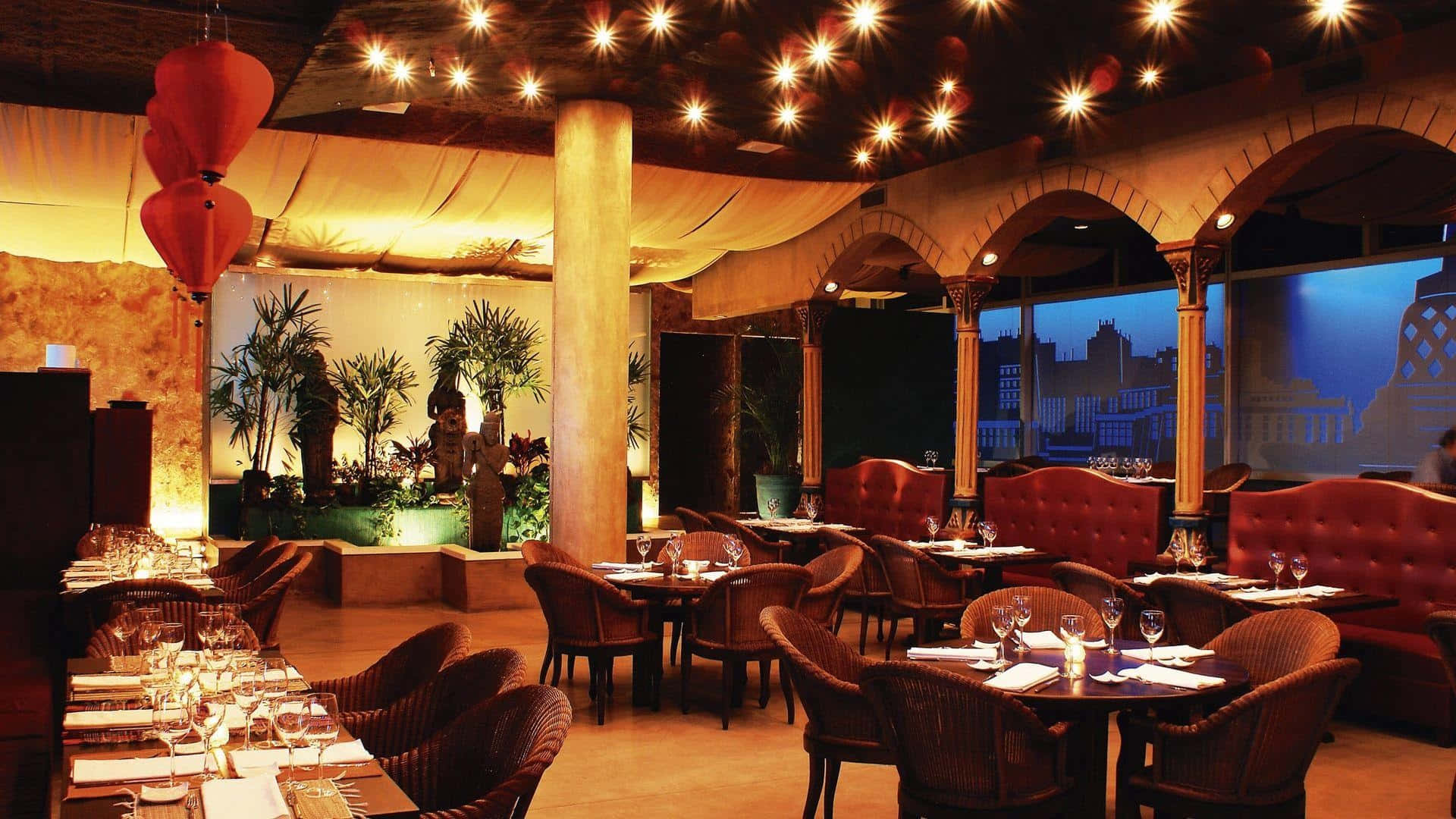 Elegant restaurant with red seating and hanging lanterns overlooking a city at dusk. — Restaurant Background