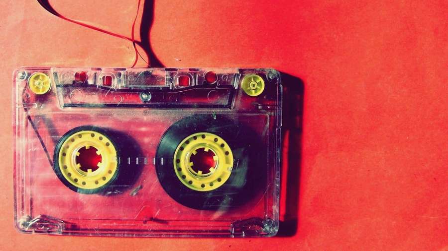 Et klart kassettbånd med gule spoler på en rød bakgrunn. — Retro Music Bakgrunner