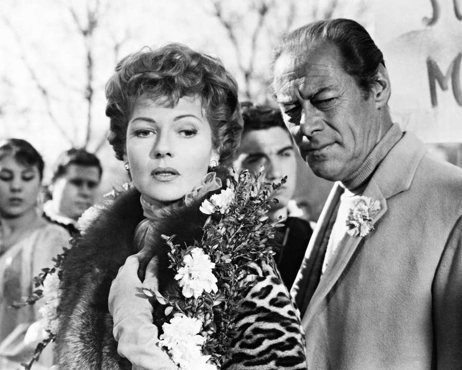 Frau mit Pelzkragen hält Blumen neben einem Mann im Anzug mit Blumenboutonniere. — Rex Harrison Bilder