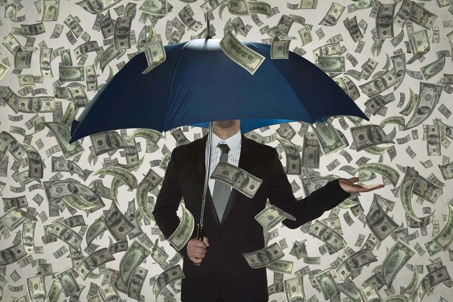 Man in suit holding blue umbrella as money falls around him. — Rich Background