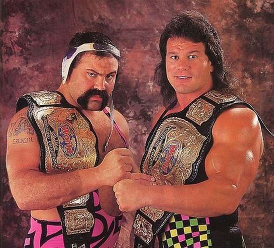 Two wrestlers in colorful outfits lock fists while wearing championship belts. — Rick Steiner Wallpaper