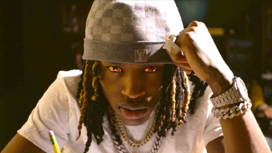 Young man with glowing eyes adjusting a checkered cap and wearing gold chains. — Rip King Von Background