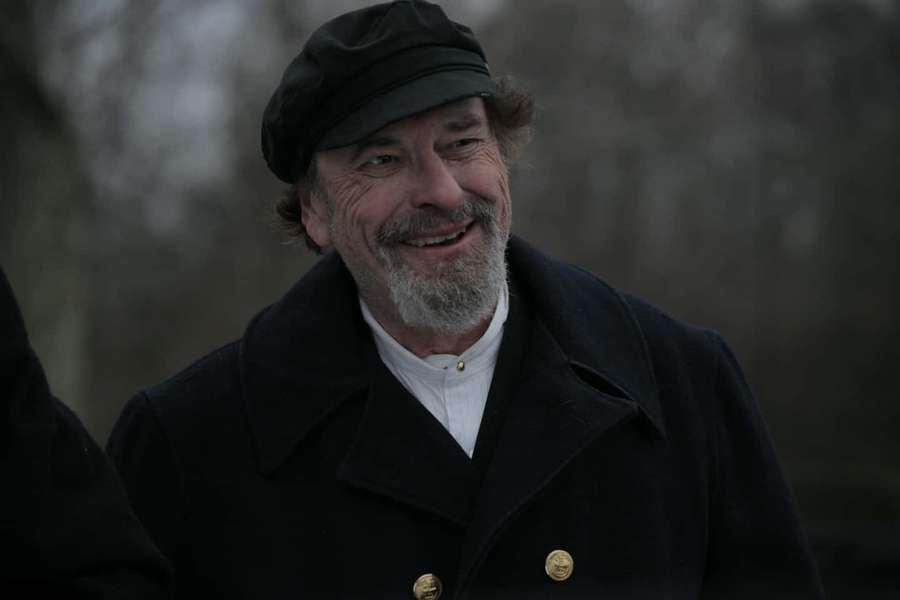 An older man with a gray beard and black cap smiles warmly in a winter coat. — Rip Torn Wallpaper