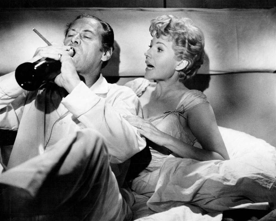 Man drinking from bottle while woman looks on in bed — Rita Hayworth Background