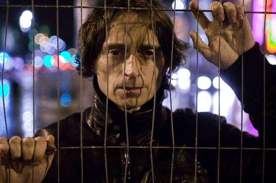 Mann greift nachts Metallstangen mit verschwommenen Stadtlichtern hinter sich. — Robert Carlyle Bilder