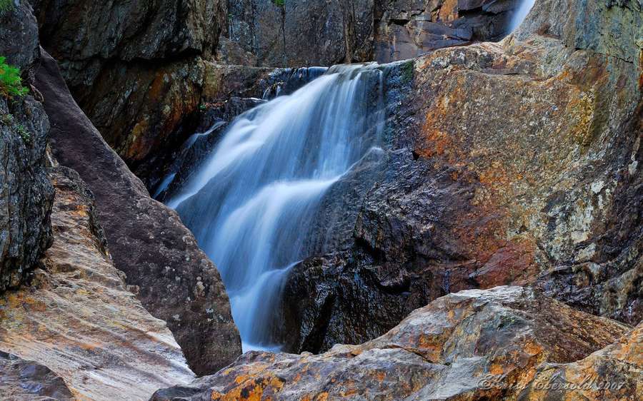 Wasserfall, der über moosbewachsene Felsen in einer Bergschlucht fließt — Rock Wallpaper