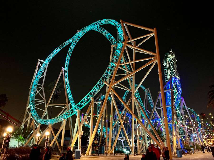 Illuminated roller coaster at night with visitors walking nearby. — Roller Background