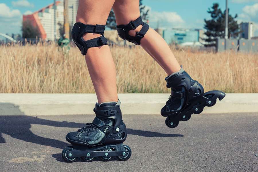 Person skating on pavement with knee pads and black inline skates in sunny urban setting. — Rollerblading Wallpaper
