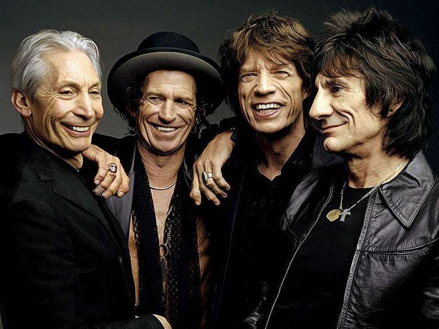 Four smiling men in rock band attire posing for a photo. — Rolling stones Background