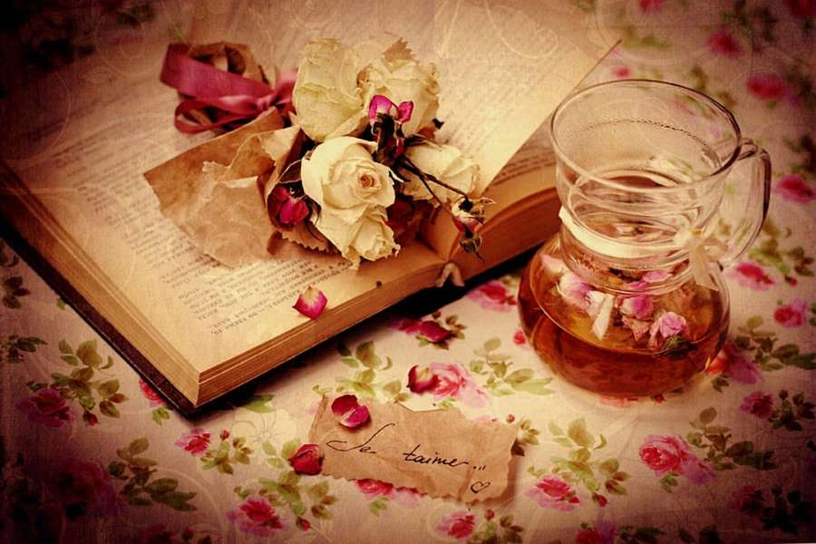 Vintage book with dried roses and rose tea on floral tablecloth. — Romantic Aesthetic Wallpaper