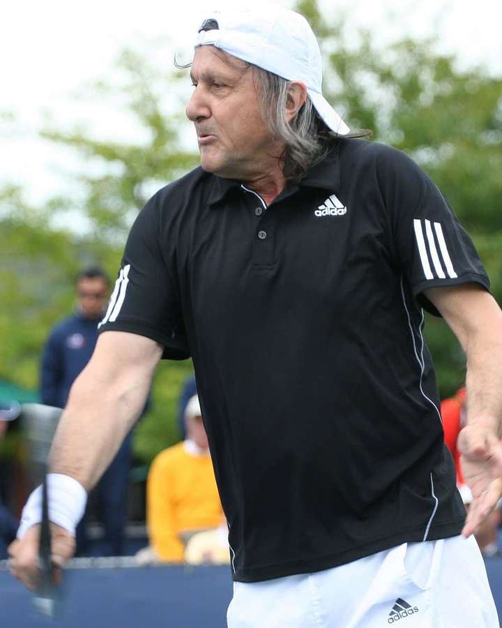 Jogador de tênis de camiseta preta Adidas e boné branco no meio do swing na quadra. — Romênia Papéis de Parede