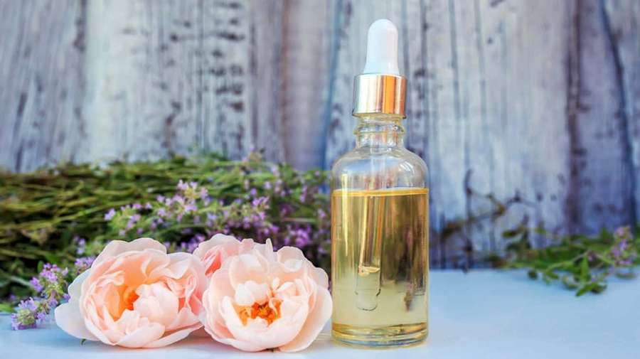 Glass bottle of essential oil with pink peonies and lavender on wooden background — Rose Oil Wallpaper