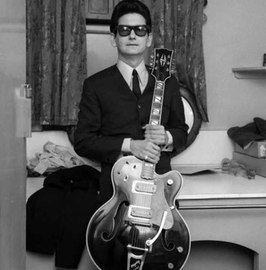 Man in suit and sunglasses holding electric guitar in vintage room. — Roy Orbison Wallpaper
