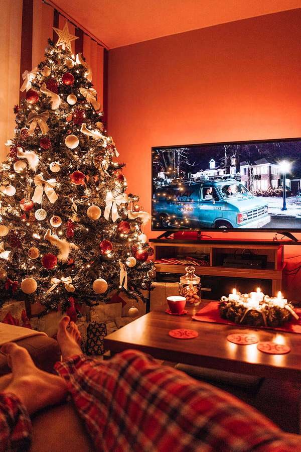 Gemütliche Füße in kariertem Schlafanzug schauen neben einem geschmückten Weihnachtsbaum mit Kerzen fern. — Rustikal Wallpaper