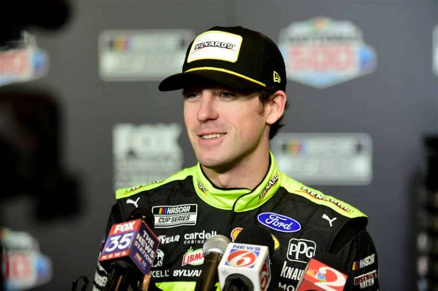 NASCAR driver in racing suit speaks to press at media event. — Ryan Blaney Wallpaper