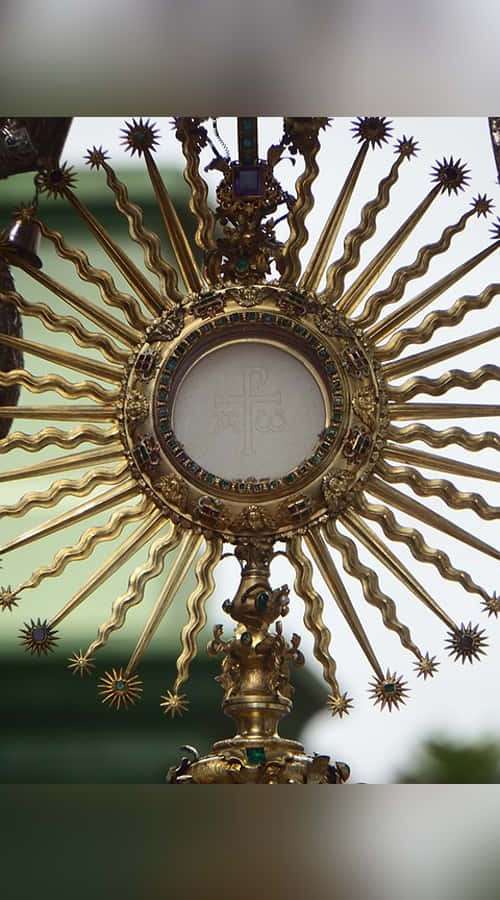 Golden religious monstrance with sunburst rays and embedded jewels displaying a sacred host. — Sacrament Wallpaper