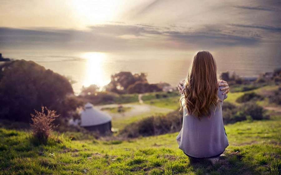 Woman sitting on grassy hill watching ocean sunset — Sad Background