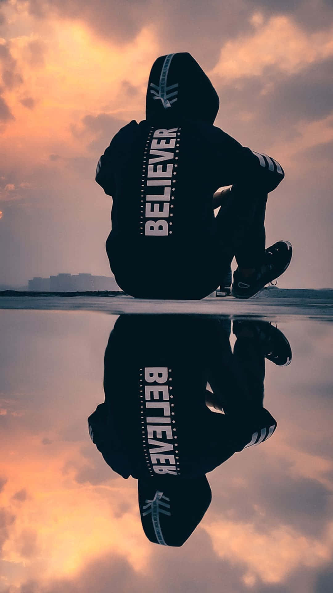 Silhouette einer Person in einem Believer-Hoodie, die am Wasser sitzt, mit Sonnenuntergangsspiegelung. — Sad Boy Bilder