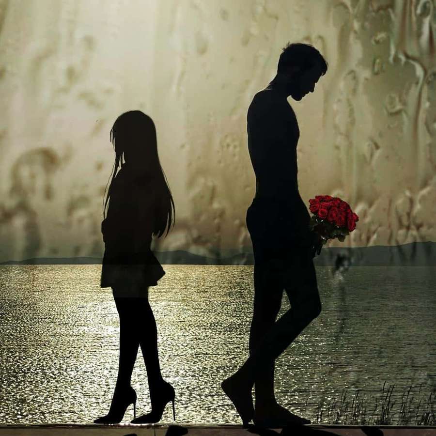 Silhouetted couple by water with man holding red roses — Sad Couple Background