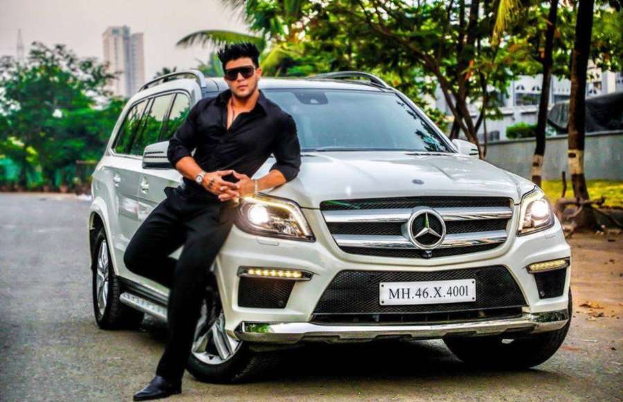 Man in black outfit posing beside white luxury SUV on city street with palm trees. — Sahil Background