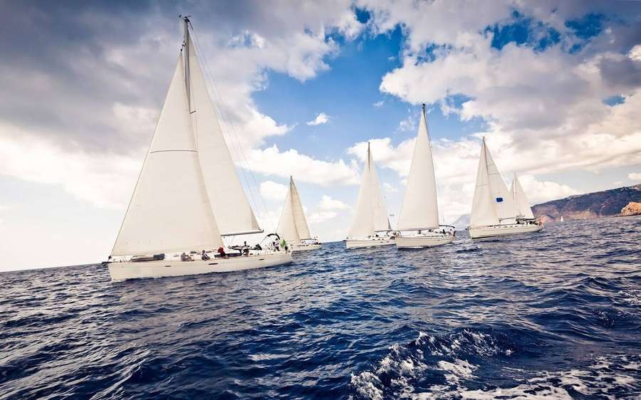 Five sailboats sailing on a blue ocean with white sails under a cloudy sky. — Sailing Background
